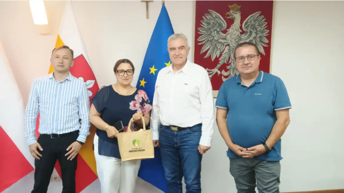 Pokaż zdjęcie: Na tle flagi Polski pozują cztery osoby.