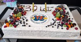 Pokaż zdjęcie: Duży prostokątny tort z napisem 30 lat Warsztatu Terapii Zajęciowej Towarzystwa Przyjaciół Dzieci, udekorowany owocami, kawałkami czekolady i bitą śmietaną. 