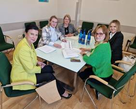 Pokaż zdjęcie: Przy stole w sali konferencyjnej siedzi pięć kobiet. Na stole leżą dokumenty.