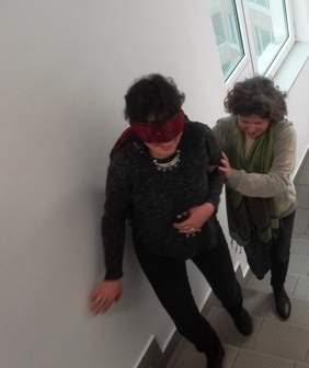 Pokaż zdjęcie: Dwie osoby idące, jedna ma zasłonięte oczy