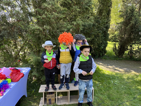 Pokaż zdjęcie: 4 chłopców stoi na podwyższeniu każdy ma na sobie jakieś śmieszne nakrycie głowy dwóch wielkie okulary. Po lewej stolik z kolorowymi akcesoriami do zdjęć. 