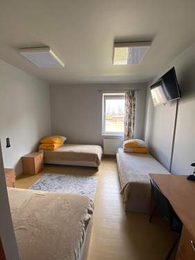 wnętrze pokoju hotelowego z trzema łóżkami, biurkiem, szafkami, telewizorem, oknem