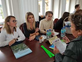 przy stole dwie kobiety i mężczyzna, naprzeciwko nich kobieta