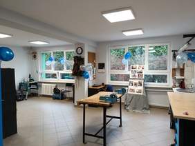 Pokaż zdjęcie: Zdjęcie pracowni stolarskiej, w której stoją trzy stoły do obróbki drewna, na ścianie wisi organizer na dłuta, sala przystrojona balonami.