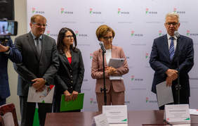 Pokaż zdjęcie: Briefing, osoby stojące na tle ścianki z napisami PFRON