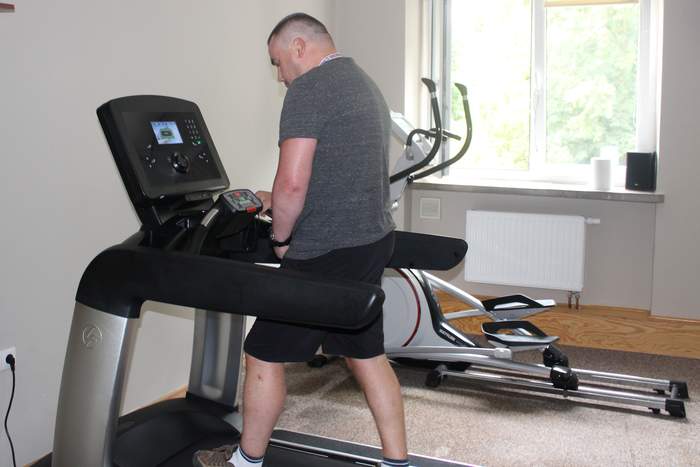 Pokaż zdjęcie: Mężczyzna w szarej koszulce i czarnych spodenkach stoi na bieżni