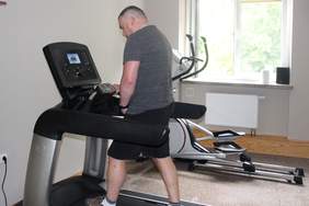 Pokaż zdjęcie: Mężczyzna w szarej koszulce i czarnych spodenkach stoi na bieżni