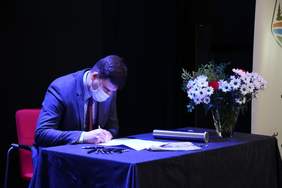 Pokaż zdjęcie: Mężczyzna nachylony nad stołem, podpisuje dokument