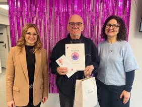 Pokaż zdjęcie: Na zdjęciu w centrum stoi mężczyzna trzymający dyplom oraz białą torbę z logo PFRON. Po lewej towarzyszy mu kobieta o długich blond włosach w okularach. Po prawej stoi kobieta z ciemnymi, kręconymi włosami w okularach, ubrana w jasnoniebieski sweter.