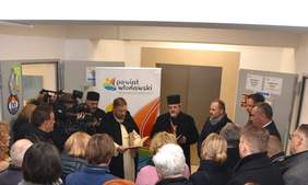 Pokaż zdjęcie: Na zdjęciu ksiądz oraz pop święcą budynek Centrum Usług Społecznych. W korytarzu stoi duża liczba osób.