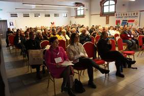 Pokaż zdjęcie: na dużej sali siedzą zaproszeni goście słuchający wystąpień