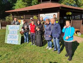 Pokaż zdjęcie: Osoby stoją przed leśną wiatą