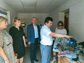 Pokaż zdjęcie: Pięć osób ogląda urządzenie do cięcia drewna, jeden z mężczyzn je dotyka