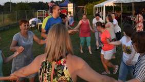 Pokaż zdjęcie: osoby tańczą i śpiewają w plenerze wszyscy trzymają się za ręce.