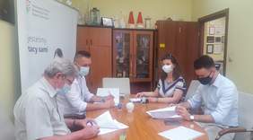 Pokaż zdjęcie: na zdjęciu: cztery osoby siedzą przy stole, podpisują dokumenty o dofinansowanie ze środków PFRON. Znajdują się w  pomieszczeniu Oddziału Łódzkiego PFRON, w tle rollup z logo PFRON. 