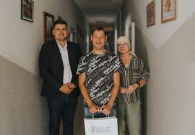 Pokaż zdjęcie: Na zdjęciu znajduje się dwóch mężczyzn i jedna kobieta. Jeden mężczyzna trzyma torbę z upominkami.