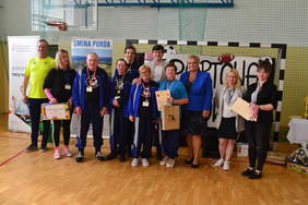 Pokaż zdjęcie: Kilkanaście osób stoi na hali sportowej. 5 osób ma na szyi medale i dyplomy