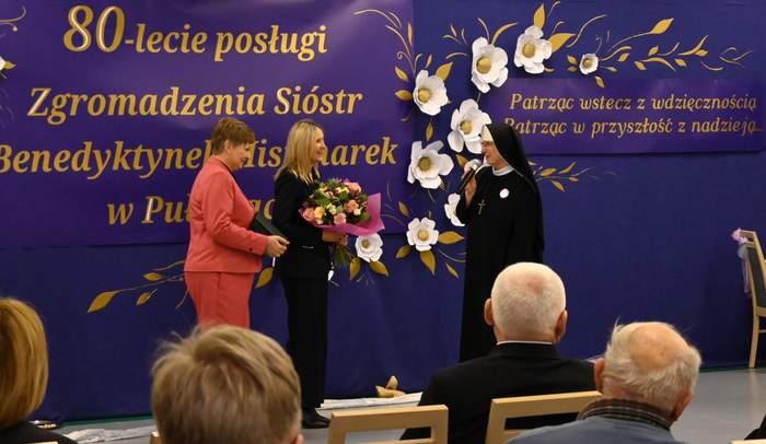 Pokaż zdjęcie: Siostrze zakonnej dwie kobiety składają życzenia, trzymają kwiaty oraz grawerton.