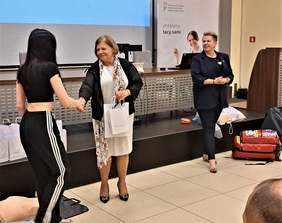 Dyrektor Oddziału PFRON Aleksandra Gierej wręcza upominki dziewczynie, w tle Pani Wicekanclerz