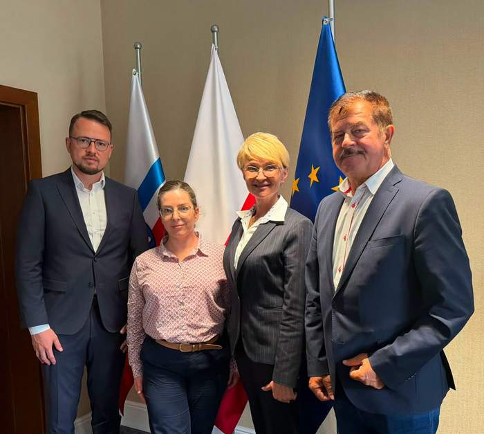 Uczestnicy spotkania w Kołobrzegu pozują do wspólnego zdjęcia na tle flag PFRON, Polski i Unii Europejskiej. Na zdjęciu: Dyrektor Zachodniopomorskiego Oddziału PFRON Bartosz Baszczyński, przedstawicielka Stowarzyszenia „Zamknięty Świat”, Prezydent Kołobrzegu Anna Mieczkowska oraz Starosta Kołobrzeski Mirosław Tessikowski.