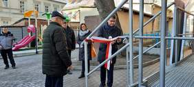 Pokaż zdjęcie: Dyrektor Oddziału Lubuskiego PFRON przecina biało-czerwoną wstęgę, obok są inne osoby, wszystko dzieje się na dworze, przy wejściu do budynku