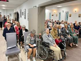 Pokaż zdjęcie: Pensjonariusze biorący udział w obchodach jubileuszu 20-lecia. Część osób siedzi na wózkach, część na krzesełkach.