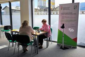 Pokaż zdjęcie: Stoisko informacyjne PFRON. Osoba zainteresowana rozmawia z ekspertem PFRON. Na stoliku dostepne są ulotki oraz informatory PFRON.