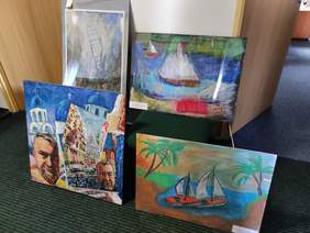 Pokaż zdjęcie: Na podłodze i na krzesłach poustawiane są prace plastyczne. Sa to cztery obrazy z kategorii malarstwo.