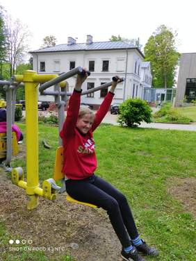 Pokaż zdjęcie: Dziewczyna ubrana w różową bluzę i dresy siedzi na drążku do ćwiczeń