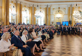 Pokaż zdjęcie: w sali zamku kilkaset siedzących osób. Wszyscy sa odświętnie ubrani. Piekne złote wnętrze dużej sali.