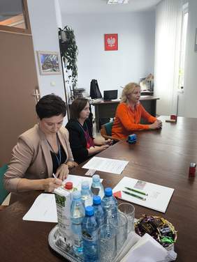 Pokaż zdjęcie: Zdjęcie trzech kobiet siedzących przy stole w gabinecie Pani Dyrektor, jedna z kobiet podpisuje umowę.
