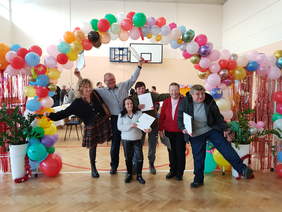 Zdjęcie 6 uśmiechniętych osób, na tle balonów, w tle widać innych uczestników wydarzenia