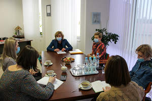 Sześć kobiet siedzących w maseczkach przy brązowym stole, przed nimi leżą dokumenty