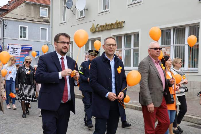Pokaż zdjęcie: Obok siebie z pomarańczowymi balonami w rękach idą ulicami miasta Burmistrz Wschowy, Wicestarosta Wschowski oraz Dyrektor Oddziału Lubuskiego PFRON, w tle idą inni uczestnicy