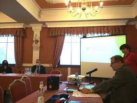 Pokaż zdjęcie: Za stołem prezydialnym siedzi Tomasz Maruszewski, na sali siedzący uczestnicy konferencji.