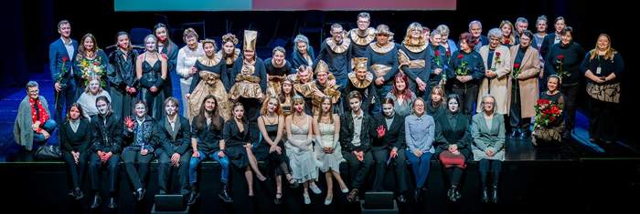 Pokaż zdjęcie: Na scenie siedzi wiele ucharakteryzowanych postaci.