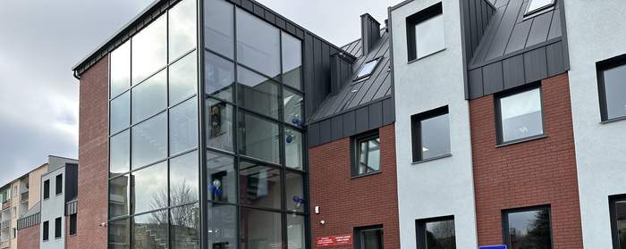 Pokaż zdjęcie: Nowy budynek z elewacją pół na pół cegła i biała ściana na zmianę. Po środku monumentalna szklana klatka schodowa z windą w środku.