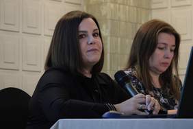 Pokaż zdjęcie: Zdjęcie dwóch kobiet siedzących koło siebie przy stole prezydialnym na konferencji, pierwsza od lewej przemawia przez mikrofon.