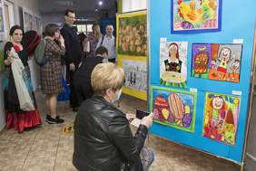 Pokaż zdjęcie: W holu budynku ludzie oglądający wystawę prac plastycznych.