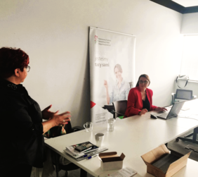 Pracownik PFRON podczas wystąpienia, za nią baner PFRON, a po lewej stronie stoi tłumaczka języka migowego