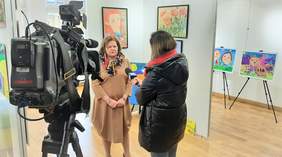 Pokaż zdjęcie: Dyrektor Oddziału Aleksandra Gierej podczas wywiadu dla TVP3 Zbliżenia, na pierwszym planie stoi kamera, na drugim Pani Redaktor i Pani Dyrektor, a w tle prace prace plastyczne na wystawie
