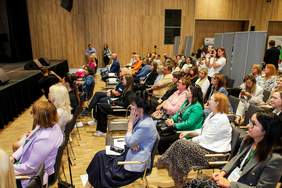 Pokaż zdjęcie: Grupa osób siedzących na krzesłach w auli. Z uwagą słucha prelegenta.