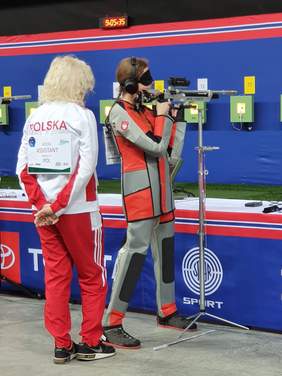 dwie kobiety uczestniczki zawodów w strzelectwie niewidomych, zawodniczka z karabinem stoi, za nią asystentka