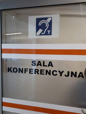 Pokaż zdjęcie: Drzwi sali konferencyjnej oznakowane kontrastową taśmą i piktogramemem pętli indukcyjnej dla słabosłyszących