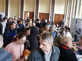 Pokaż zdjęcie: W sali konferencyjnej znajduje się duża grupa osób, która przyszła na Giełdę Pracy dla osób z niepełnosprawnością. Na sali widoczne są stoiska pracodawców, w tym także stoisko informacyjne Oddziału Wielkopolskiego PFRON.