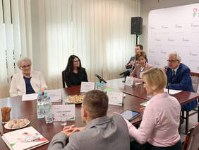 Pokaż zdjęcie: Uczestnicy briefingu siedzą przy stole konferencyjnym i rozmawiają