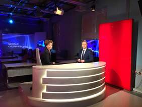 Pokaż zdjęcie: Dwie osoby za kontuarem w studiu telewizyjnym.