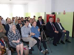 Pokaż zdjęcie: Uczestnicy spotkania siedzą na krzesełkach ustawionych w rzędach.