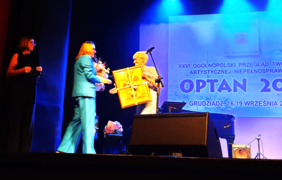 Pracownik naszego Oddziału wręcza kwiaty organizatorce przeglądu, a ona trzyma w rękach obraz ze słonecznikami