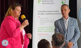 Pokaż zdjęcie: Na zdjęciu po lewej stronie widoczna kobieta z blond włosach i różowej marynarce trzymająca mikrofon w ręku, po środku widoczny baner PFRON z informacjami o CIDON, a po prawej mężczyzna w szarym garniturze - pracownik PFRON.